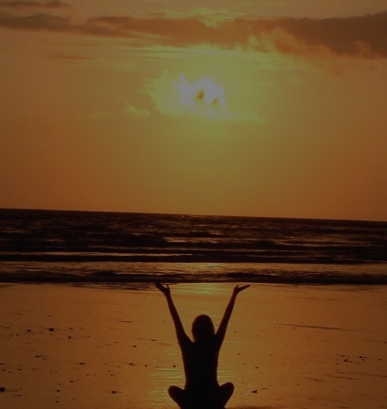 Silhouet van een vrouw in meditatie op het strand bij zonsondergang, symbool voor rust en afstemming